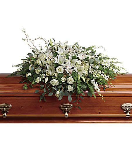 White lilies and roses casket spray arranged on top of a polished wooden coffin