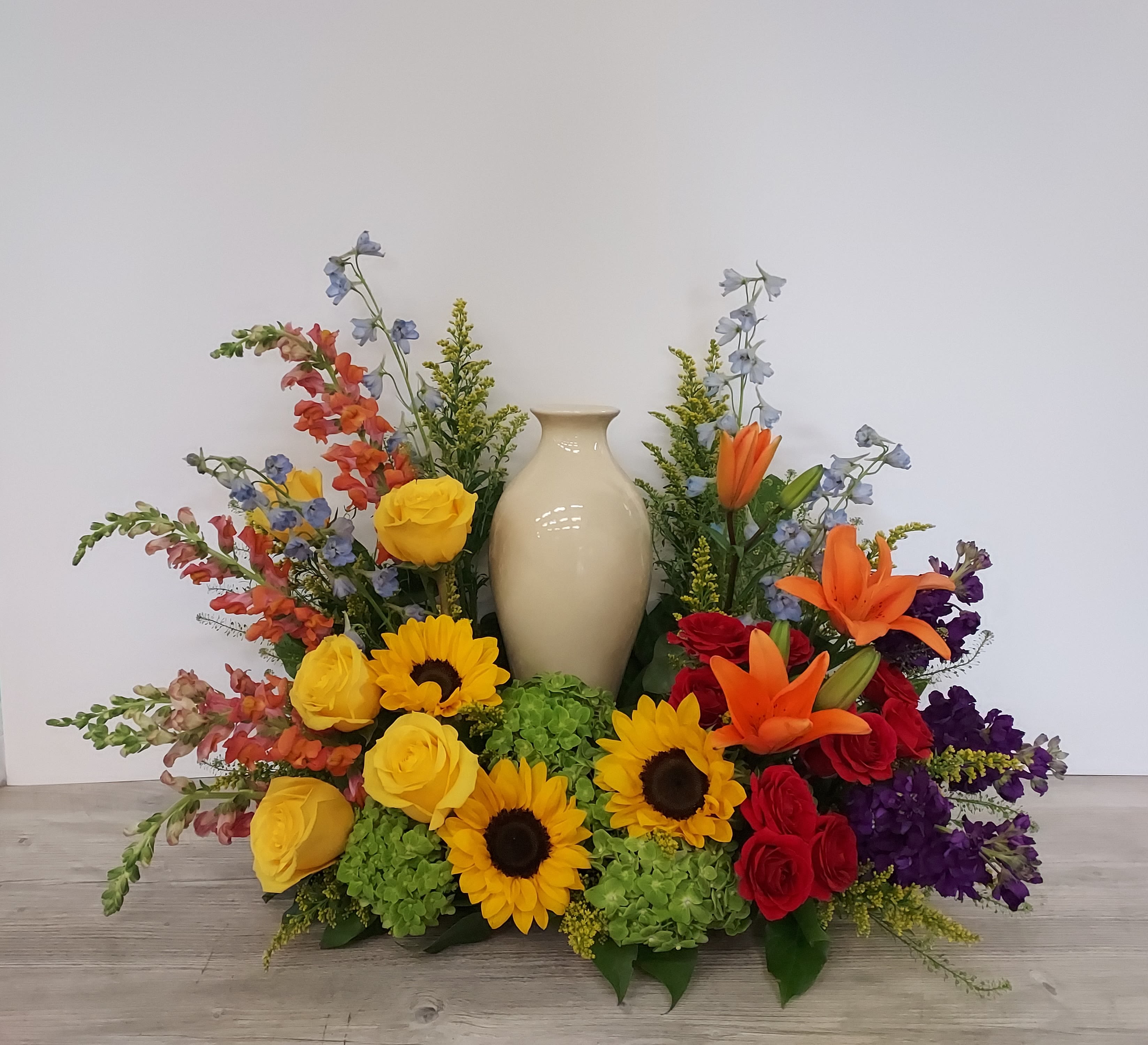 Cremation urn surrounded by bright yellow sunflowers, roses, orange lilies, and mixed colorful flowers