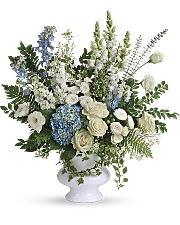 Tall white and blue flower arrangement with roses, hydrangea, and delphinium in a white pedestal vase