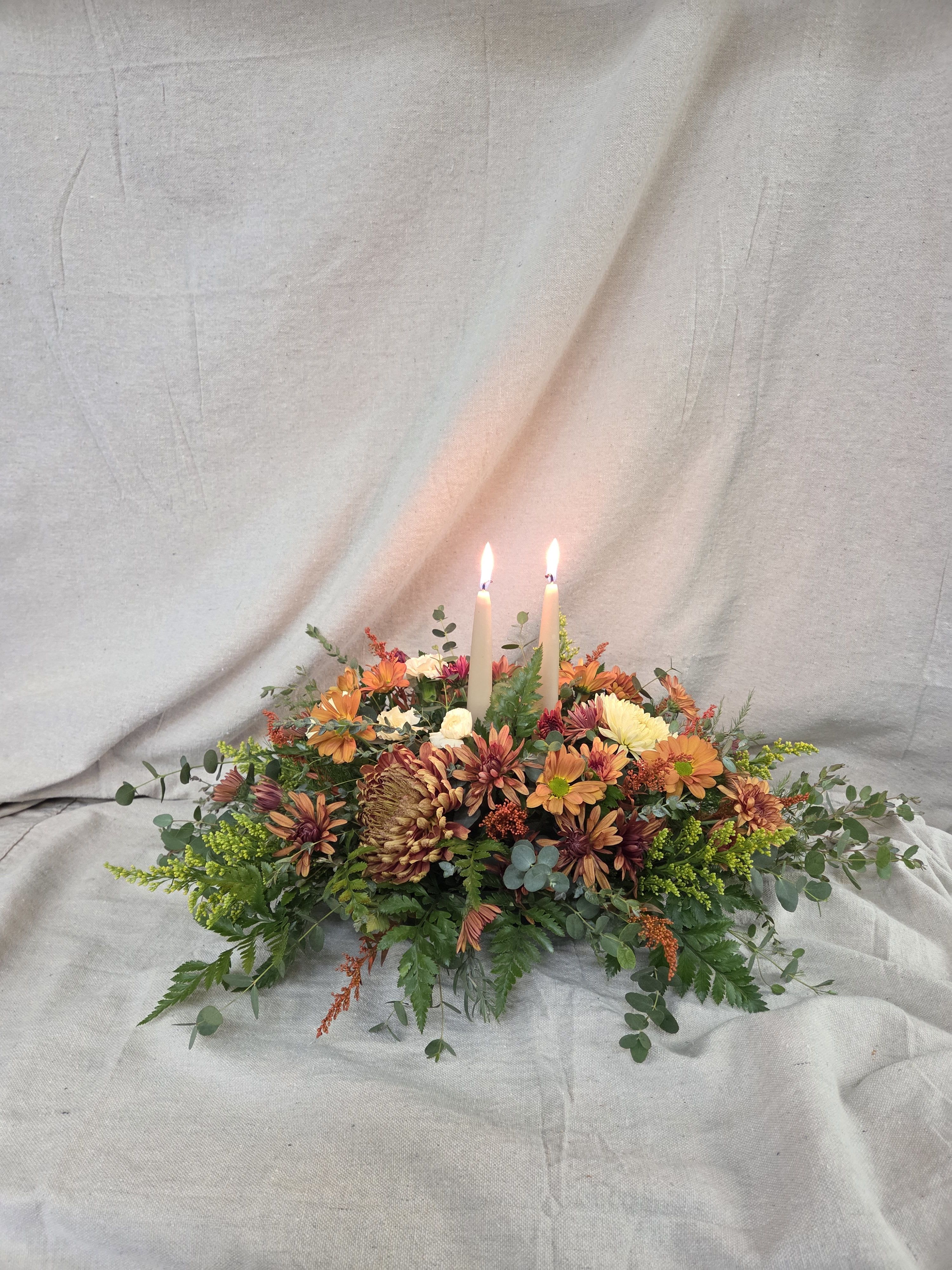 Low autumn centerpiece of orange and yellow mums with two lit ivory taper candles