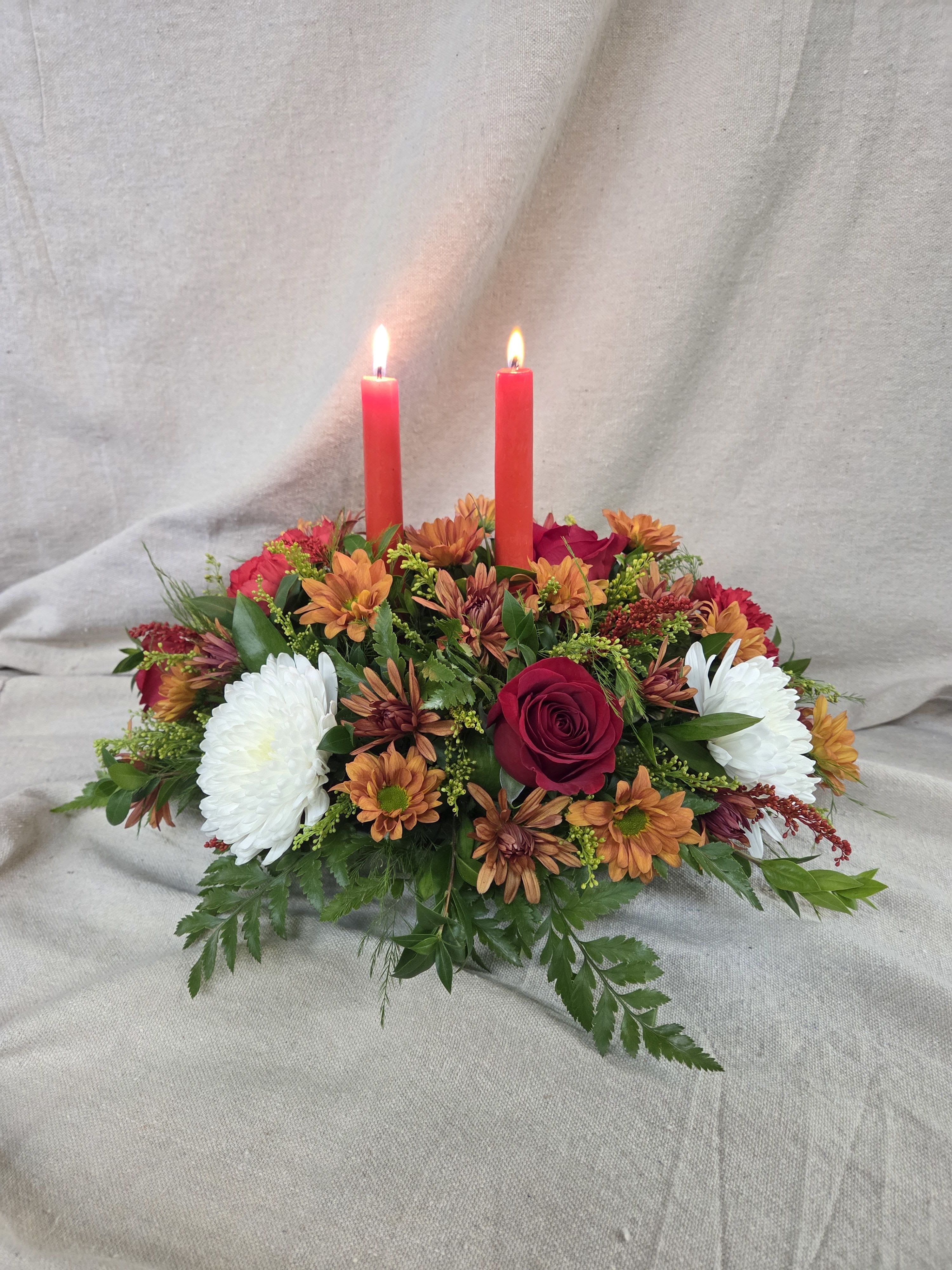 Low centerpiece with red candles, red roses, orange mums, and white mums in an oval design