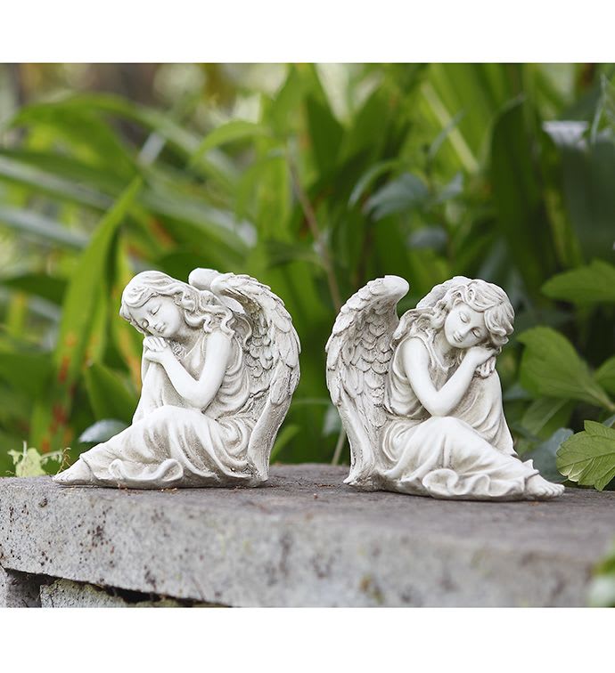 Pair of white sleeping angel figurines on a stone ledge outdoors