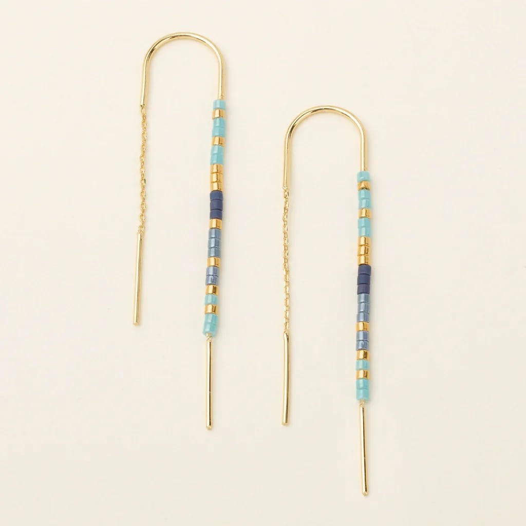 Pair of gold threader earrings with turquoise and blue beads on a light background