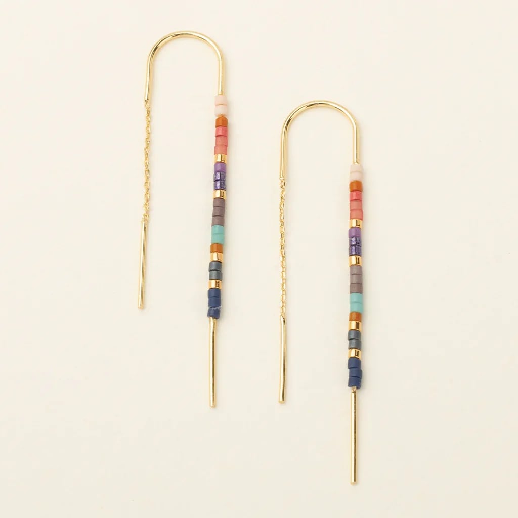 Pair of gold threader earrings with multicolor beads on a light background