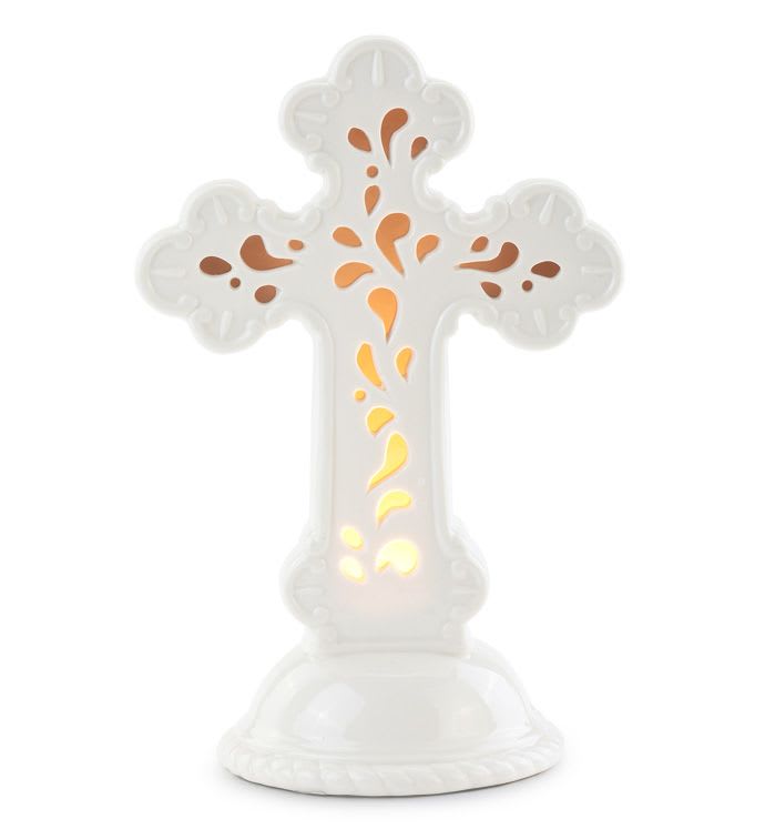 White ceramic cross with cutout pattern glowing with warm light