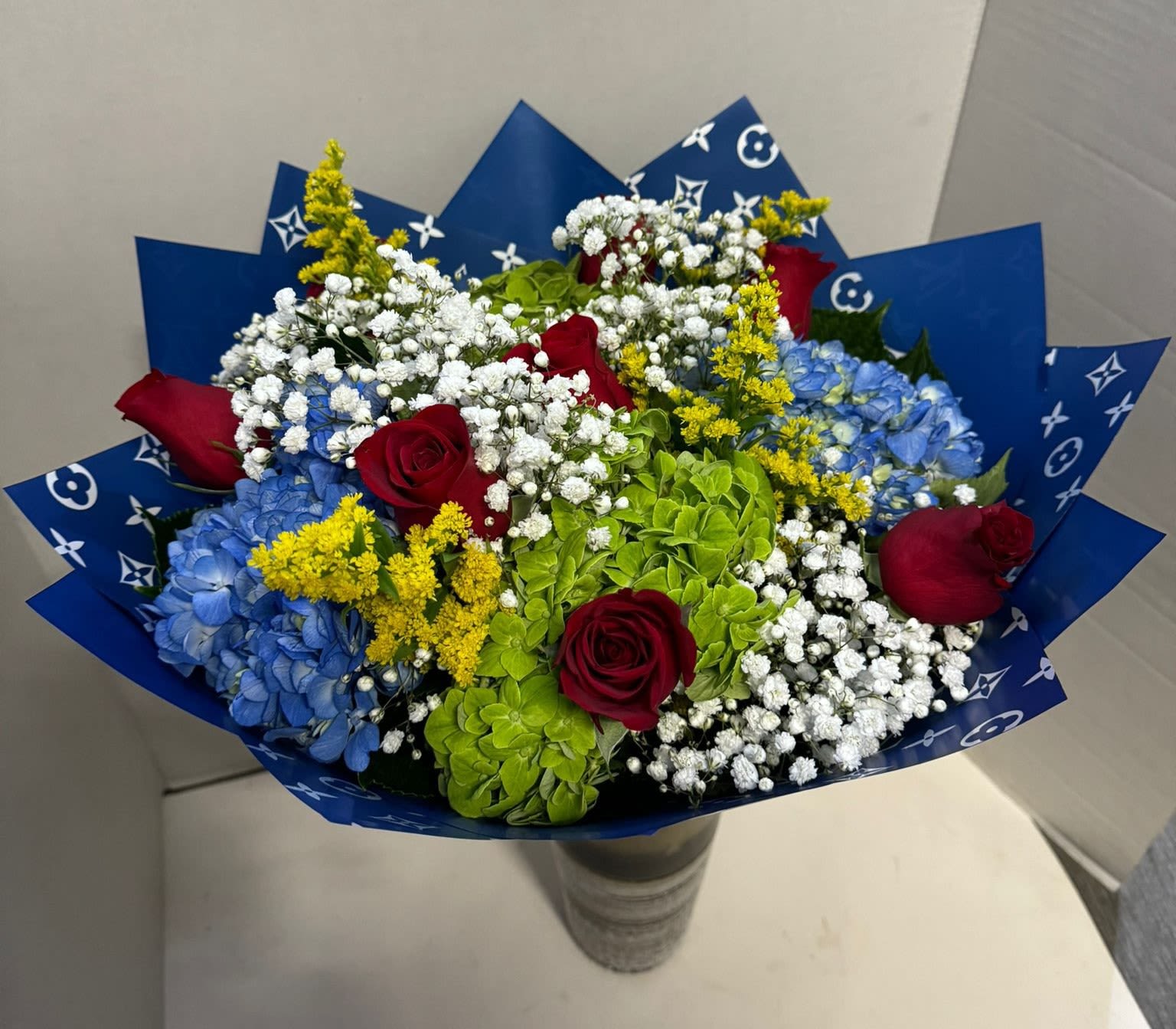 Bouquet of red roses, blue hydrangeas, and white baby's breath in blue wrap