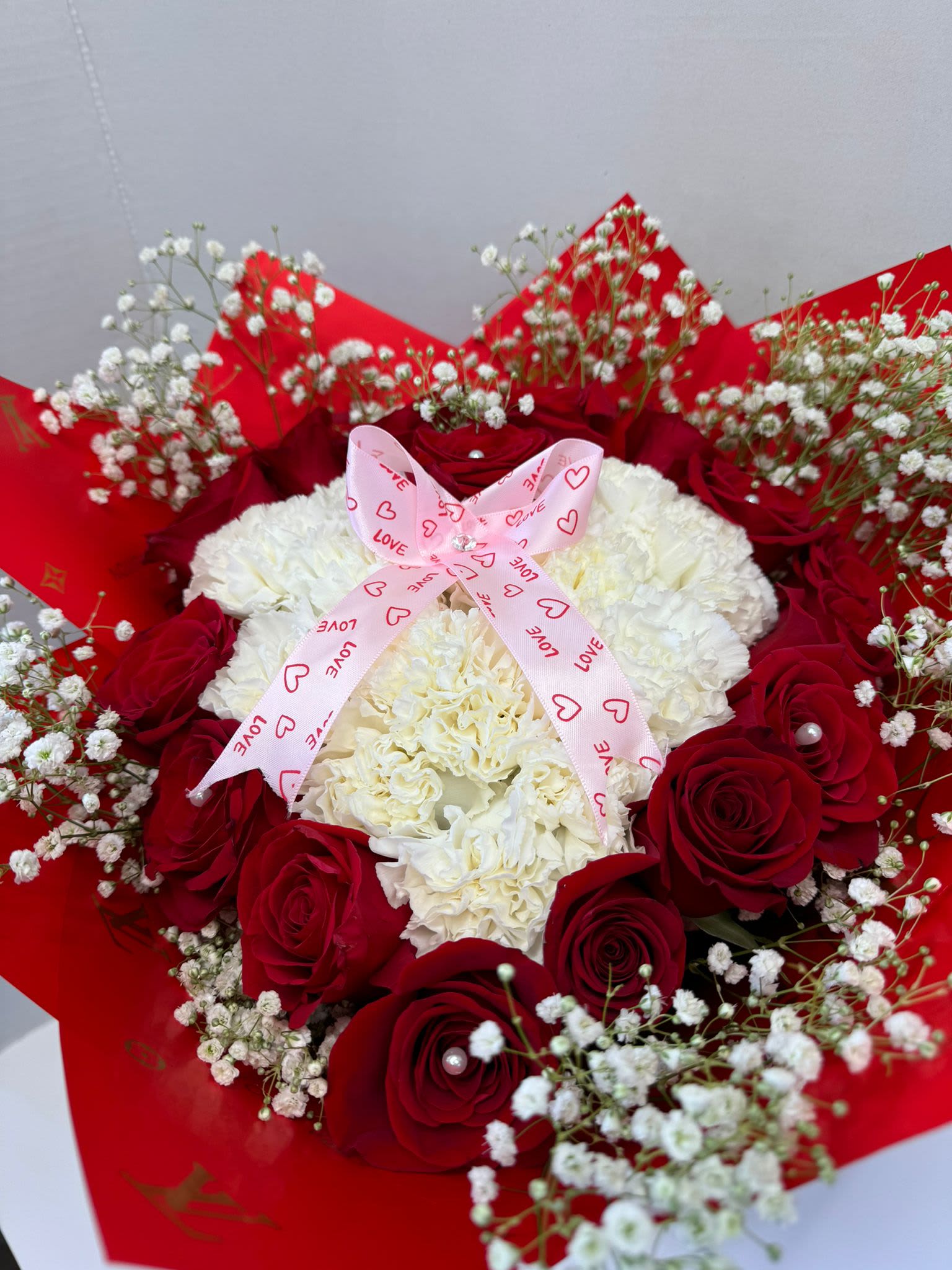 Red roses and white carnations with baby's breath, tied with a pink ribbon