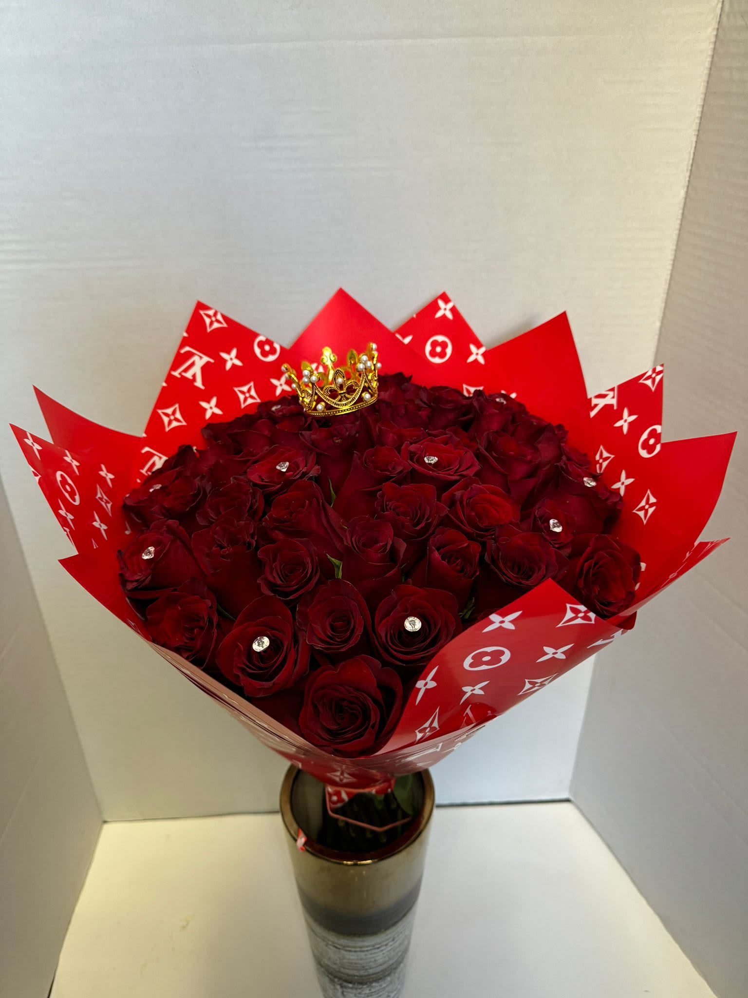 Bouquet of deep red roses wrapped in red patterned paper with a small crown topper