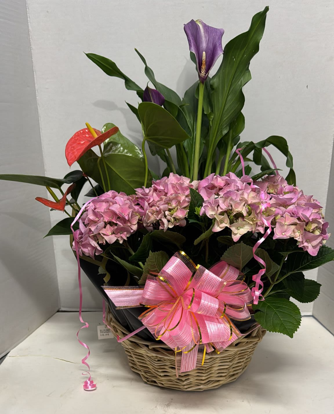 Pink hydrangeas and purple calla lilies in a wicker basket with a pink bow