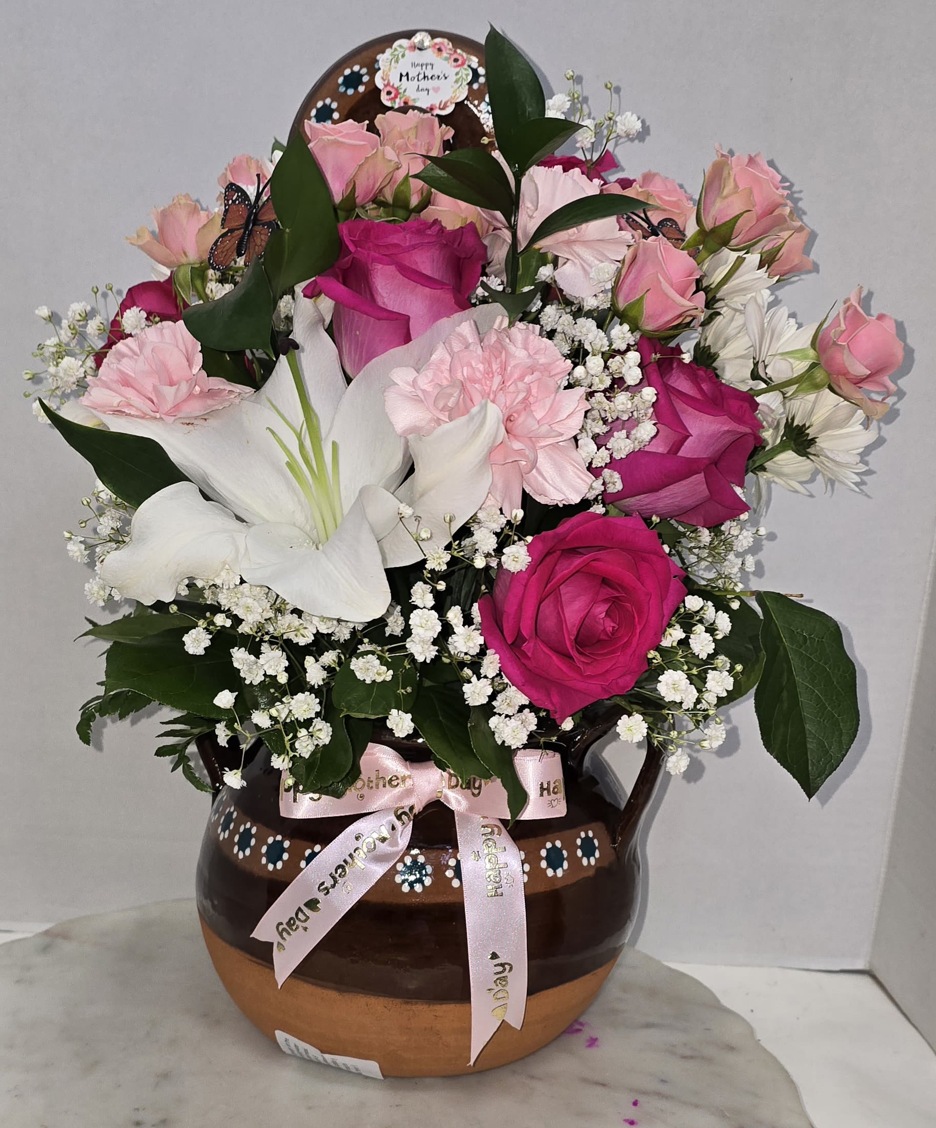 Pink and white flower arrangement in a brown ceramic vase with a ribbon