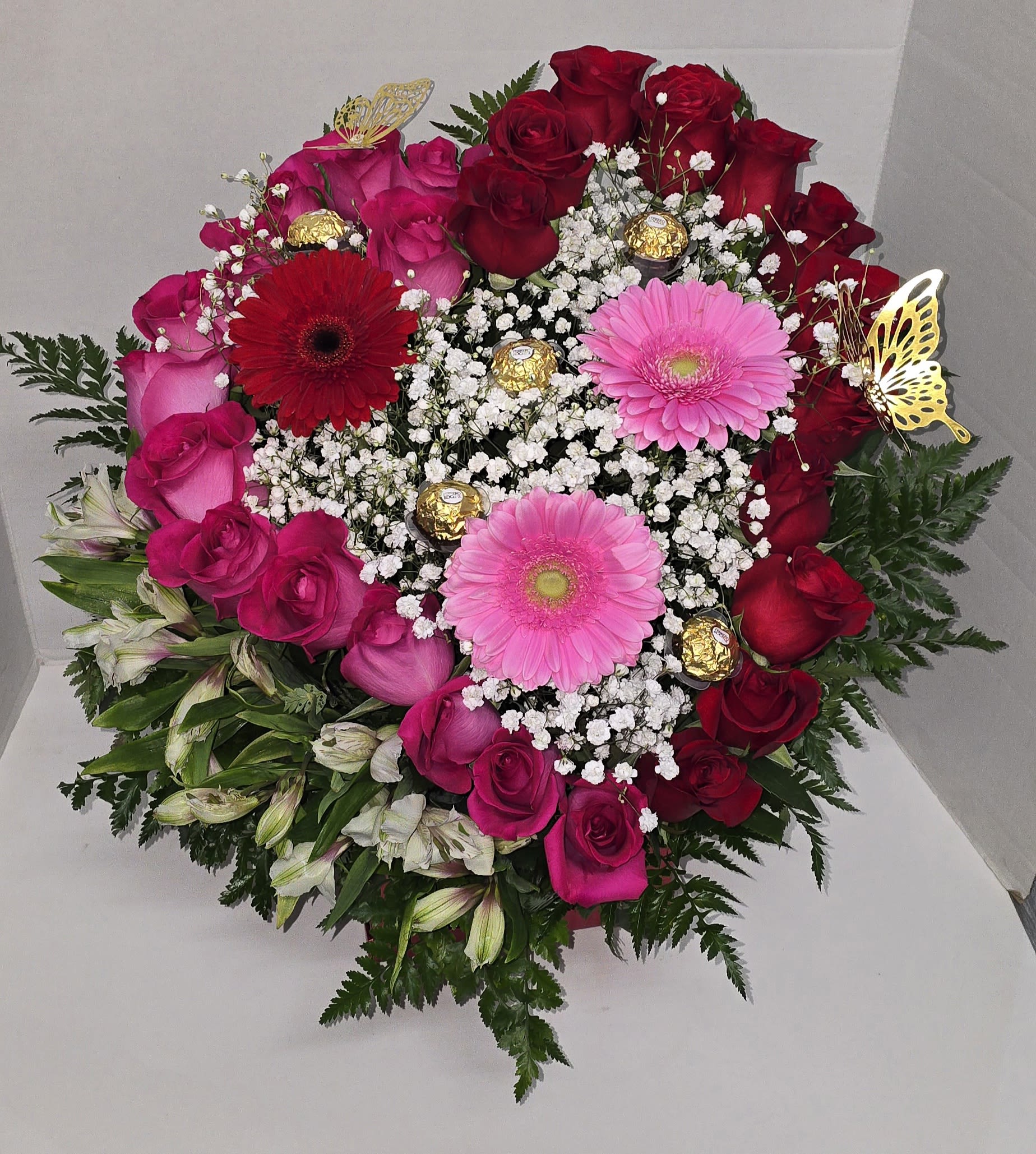 Heart-shaped bouquet of red and pink roses with gerbera daisies and chocolates