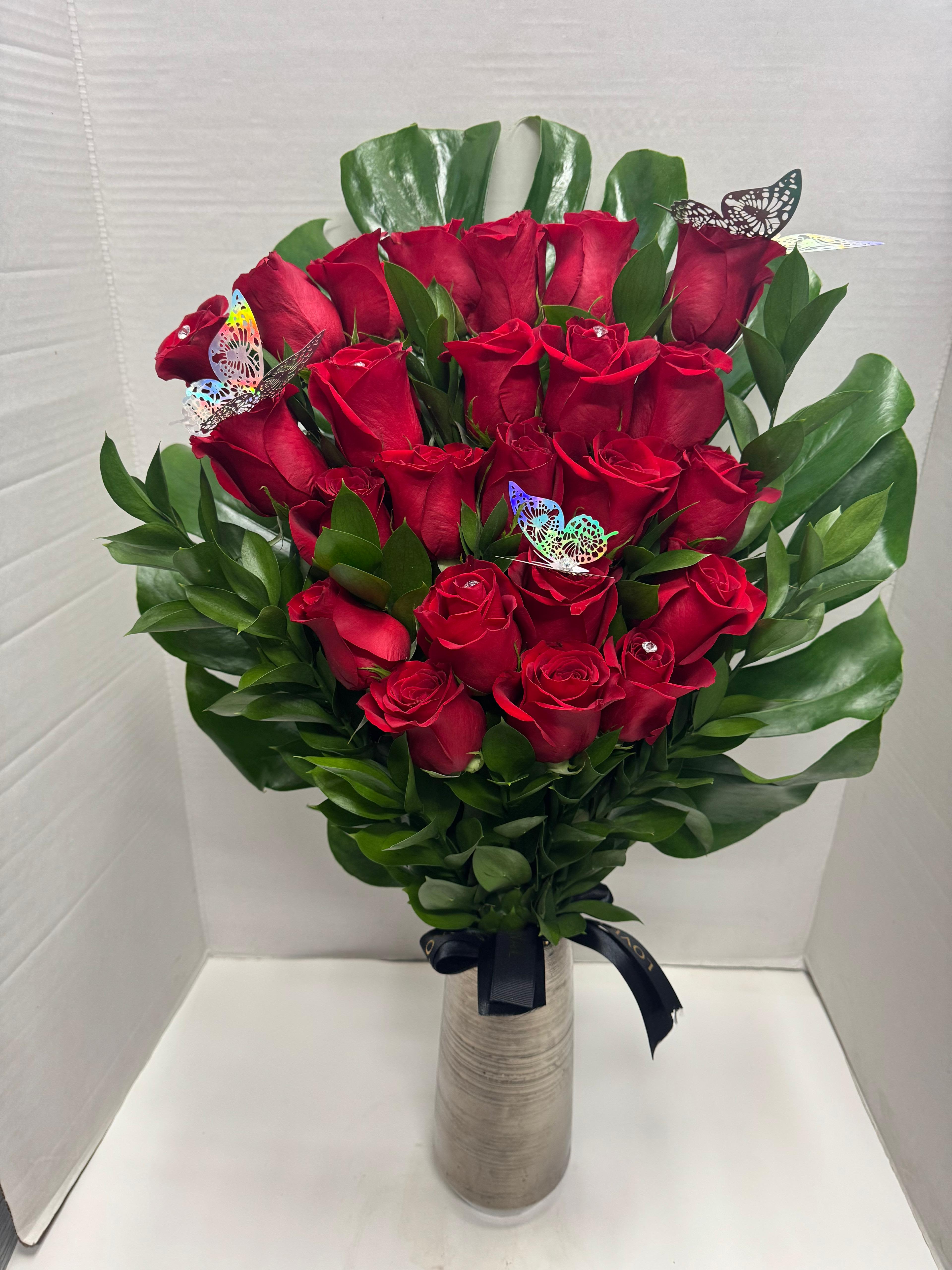 Bouquet of red roses in a tall vase with green leaves and butterfly picks