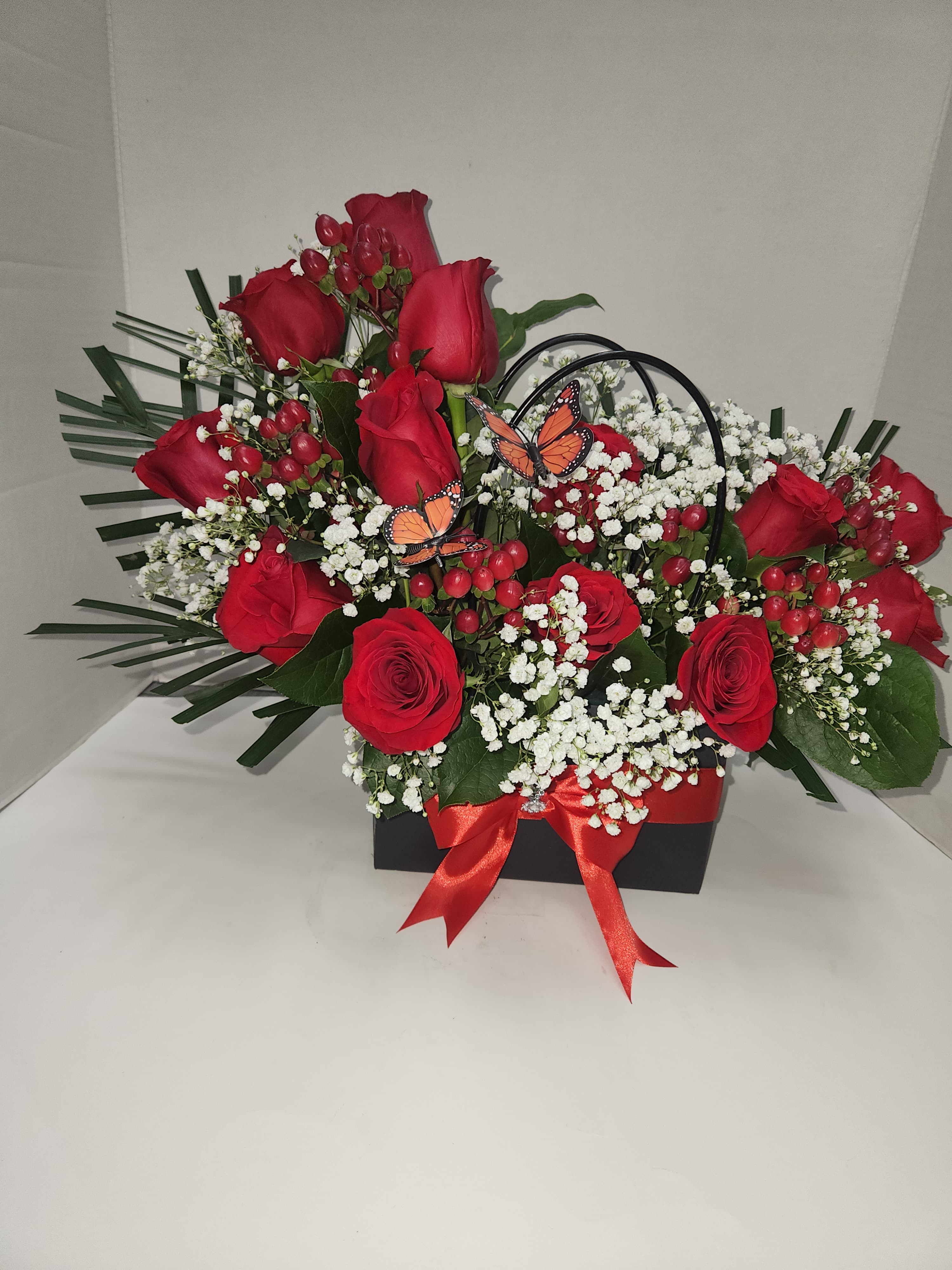 Red roses with white baby's breath in a black box, accented by butterflies and a red ribbon.