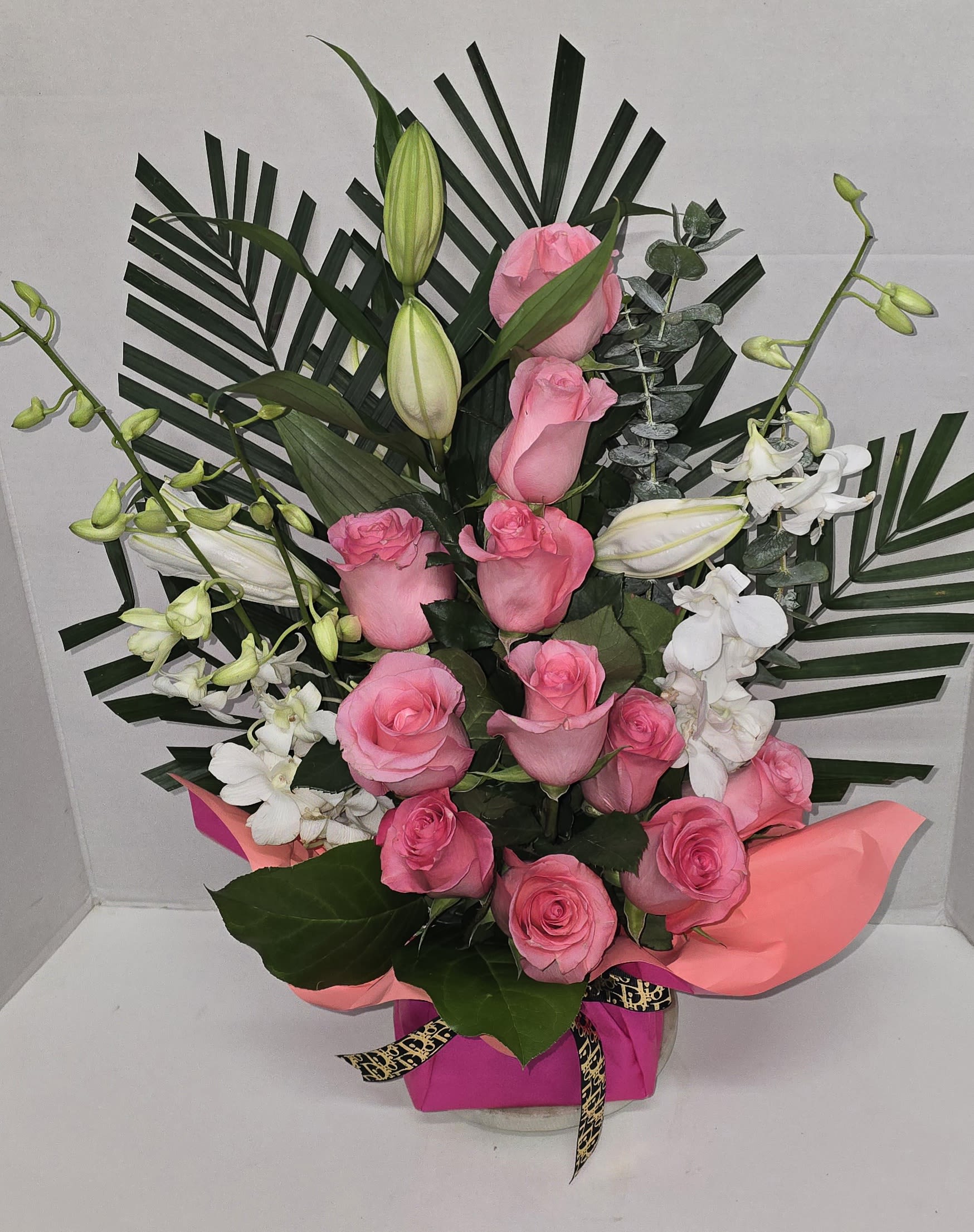 Pink roses and white lilies arranged with palm leaves in a gift box