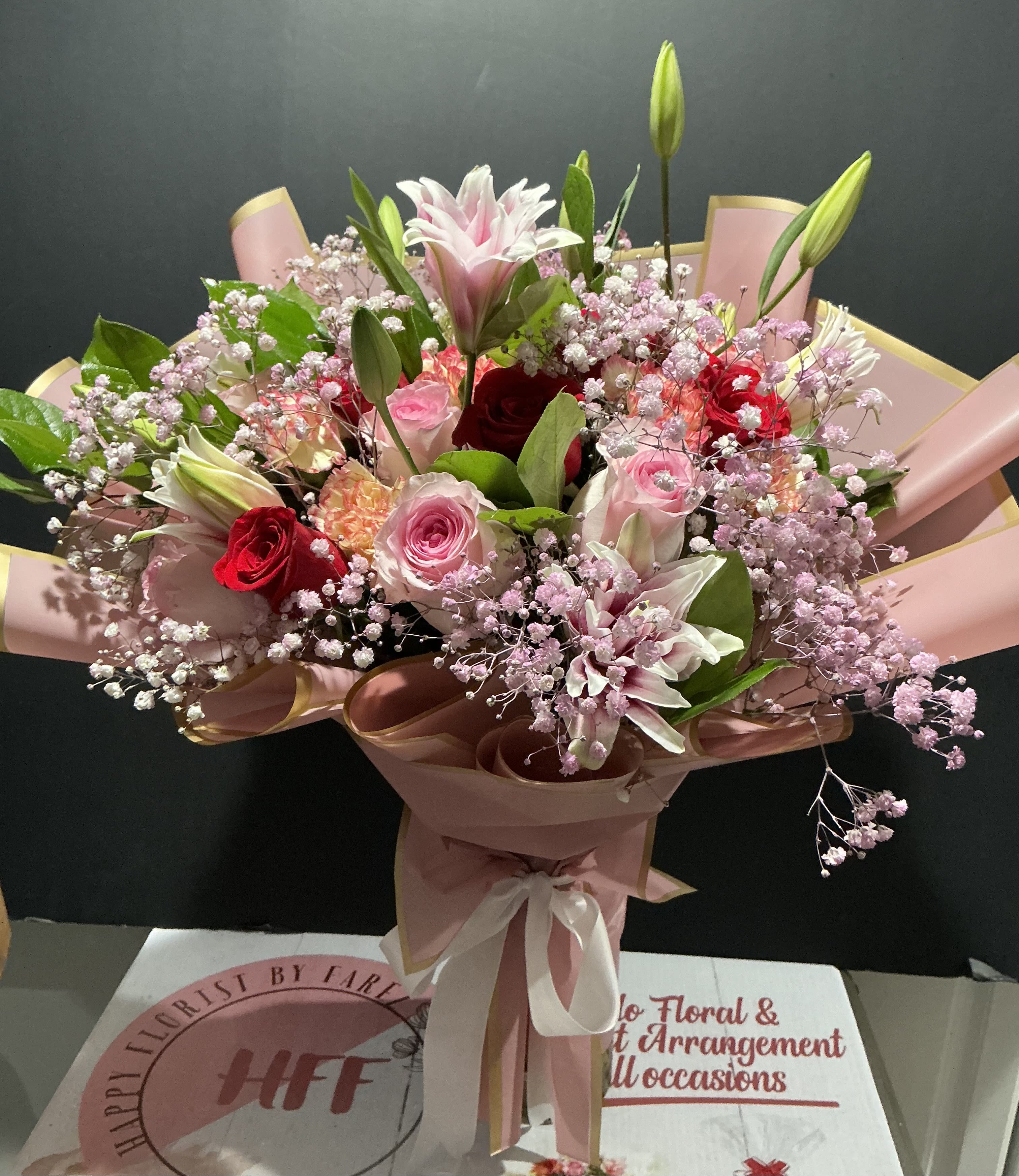 Pink and red mixed bouquet with lilies, roses, and baby's breath wrapped in pink paper