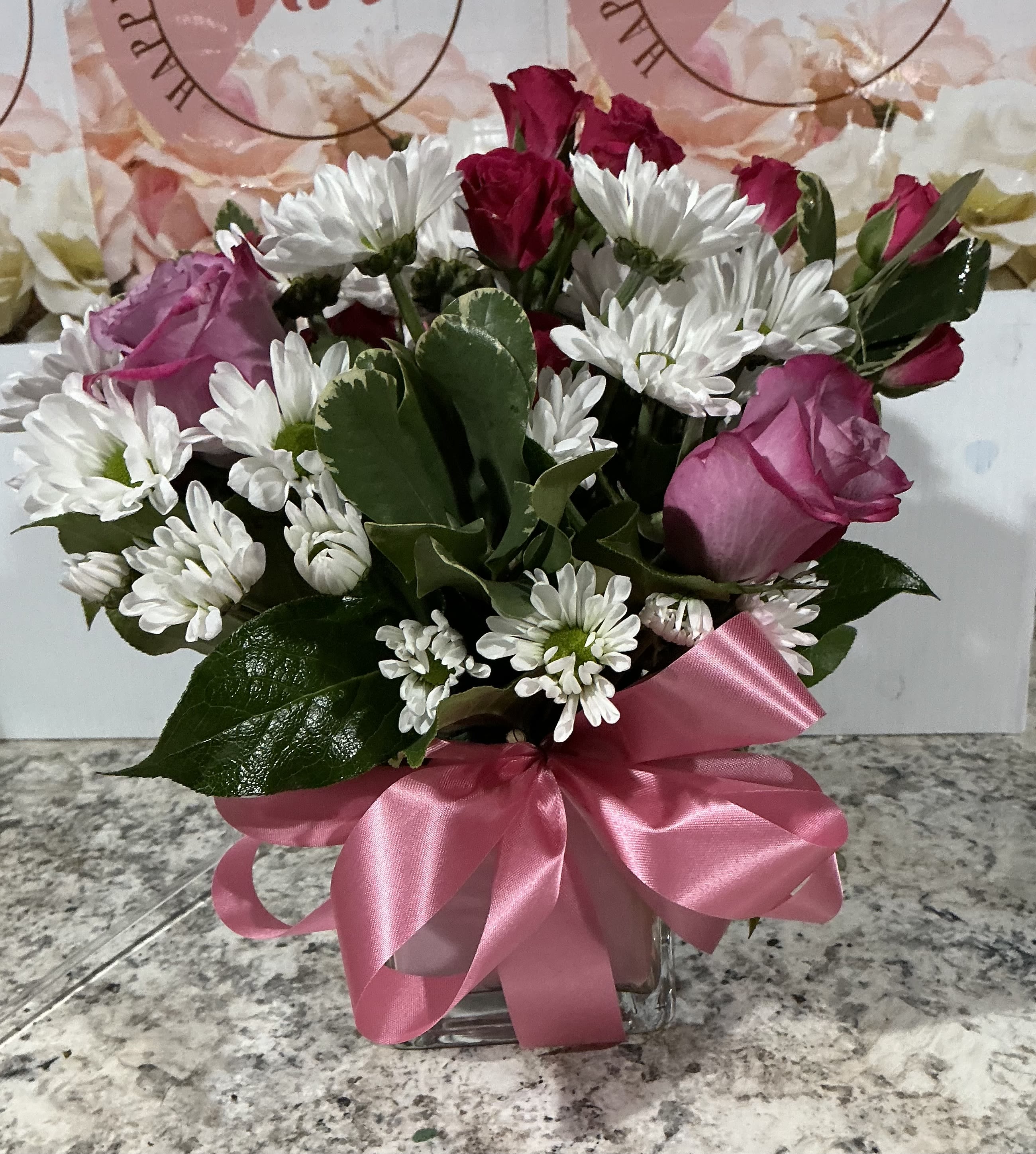 Daisy’s and hot Pink Roses  - This arrangement contains spray daisies and spray roses. This is a great birthday gift. APPROXIMATE DIMENSIONS: 9"L X 9"W x 9"H 2 hot pink roses  4 sprays roses  4 daisy’s  and greens  Square vase 