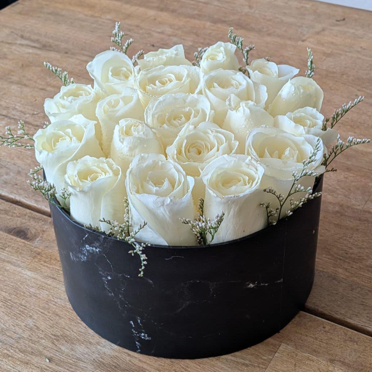 Round black box filled with tightly packed white roses and tiny white filler blooms