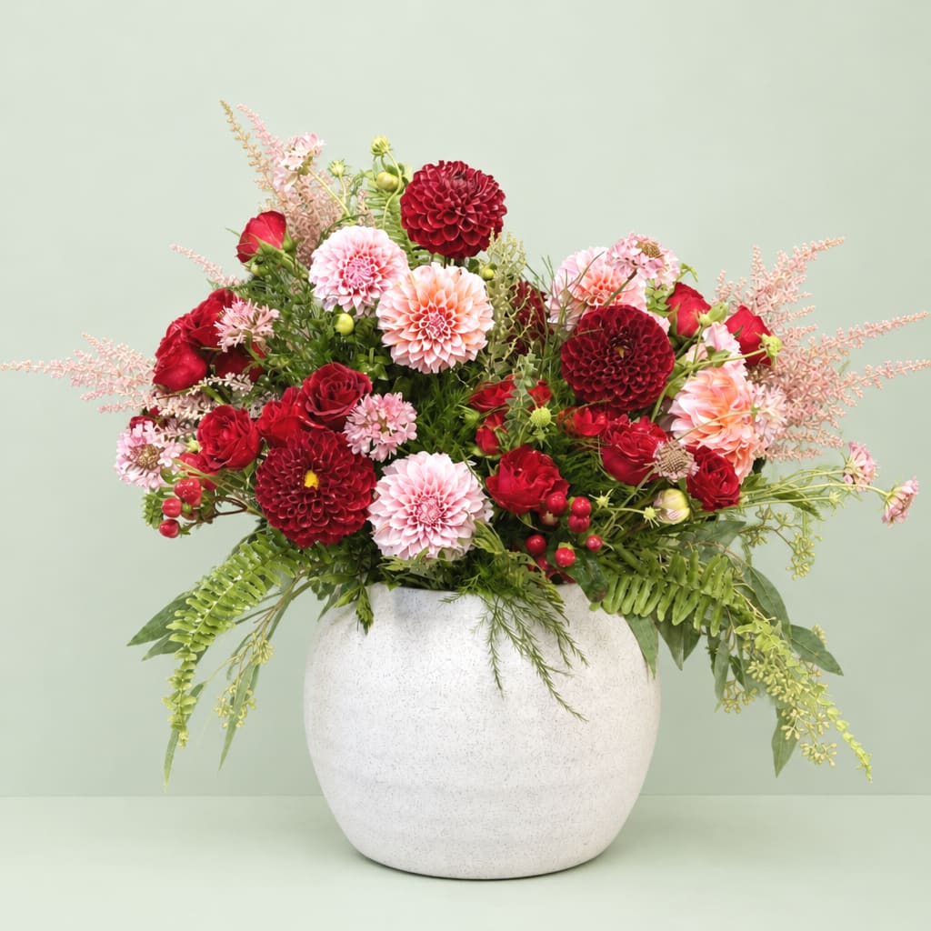 Red and pink flowers arranged in a white vase