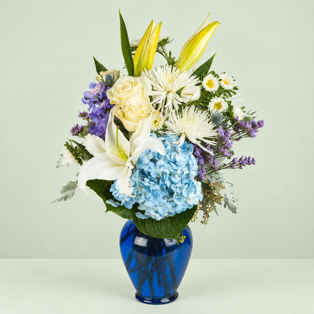 Bouquet of lilies, roses, hydrangea, and purple flowers in a blue vase