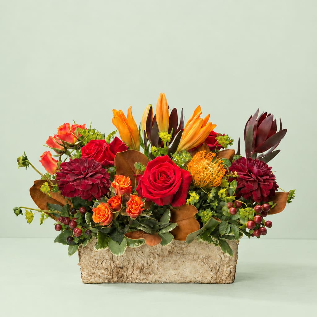 Mixed bouquet with red roses, orange lilies, and burgundy blooms in a woven basket
