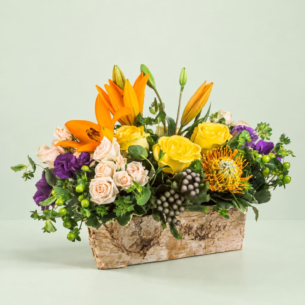 Mixed bouquet with orange lilies, yellow roses, and purple blooms in a woven basket