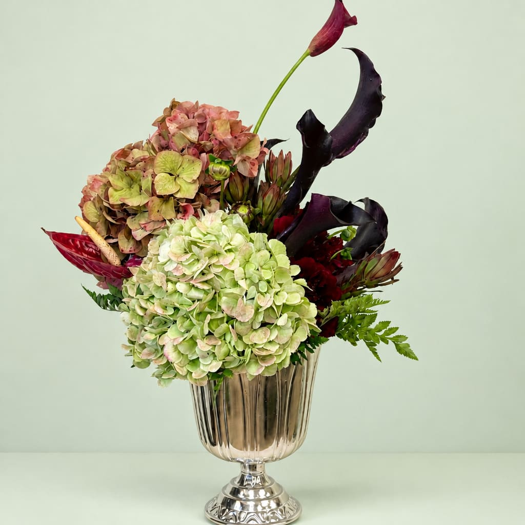 Mixed floral arrangement in a silver vase with hydrangeas and dark calla lilies