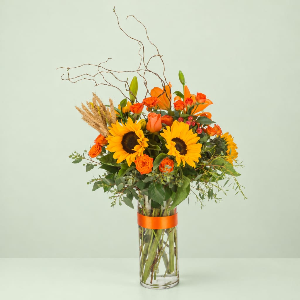 Orange and yellow bouquet in a clear glass vase with tall branches