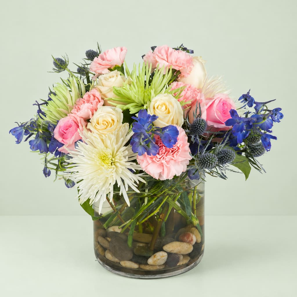 Mixed bouquet of pink, cream, and blue flowers in a glass vase