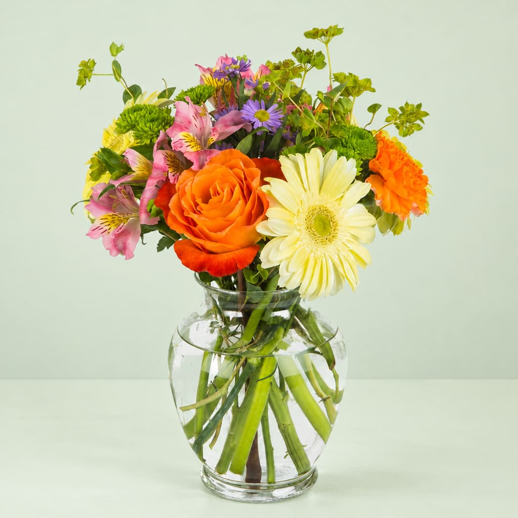 Mixed bouquet of orange, yellow, pink, and purple flowers in a clear glass vase