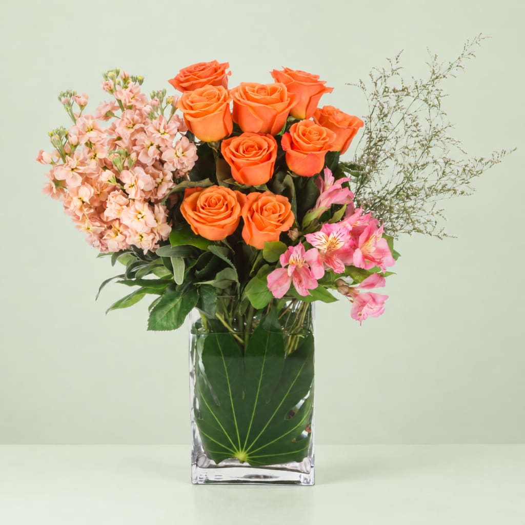 Orange roses and pink flowers arranged in a clear square vase