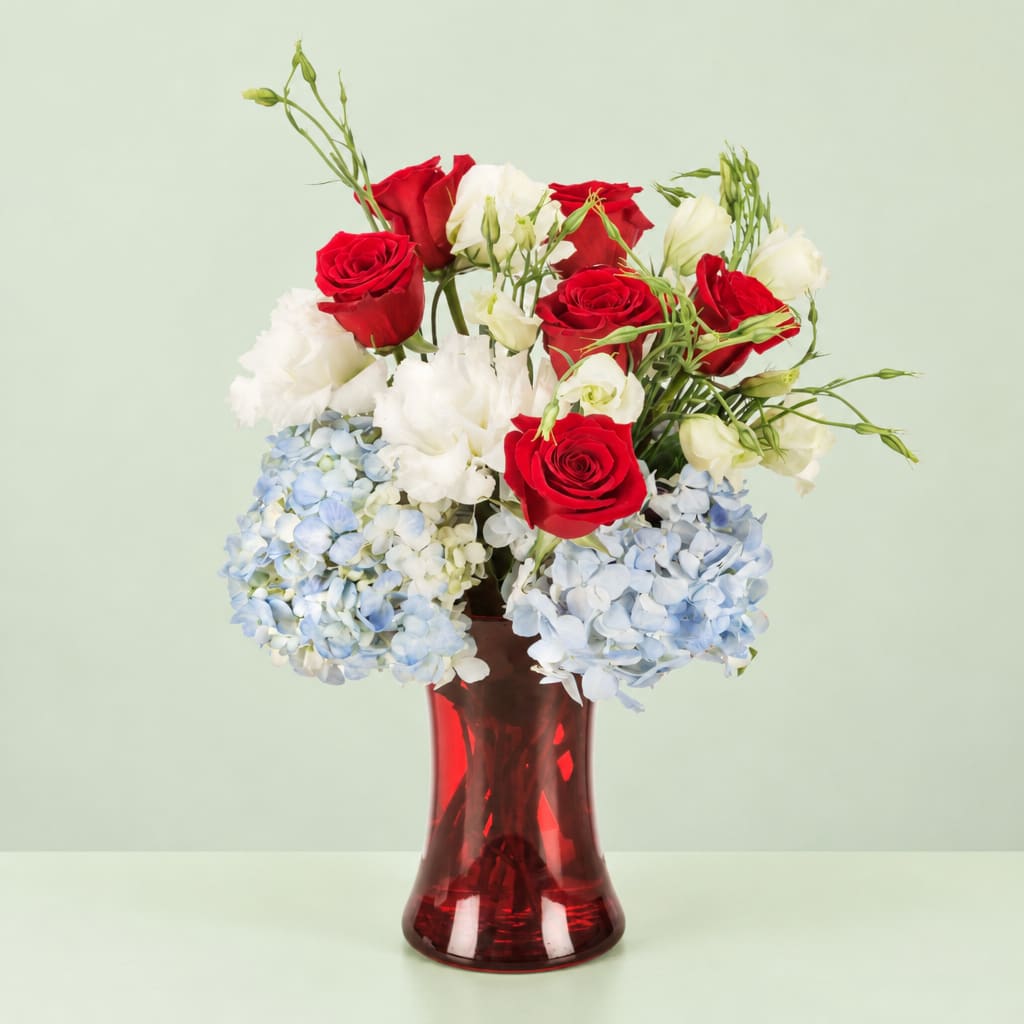 Red and white roses with blue hydrangeas in a red glass vase