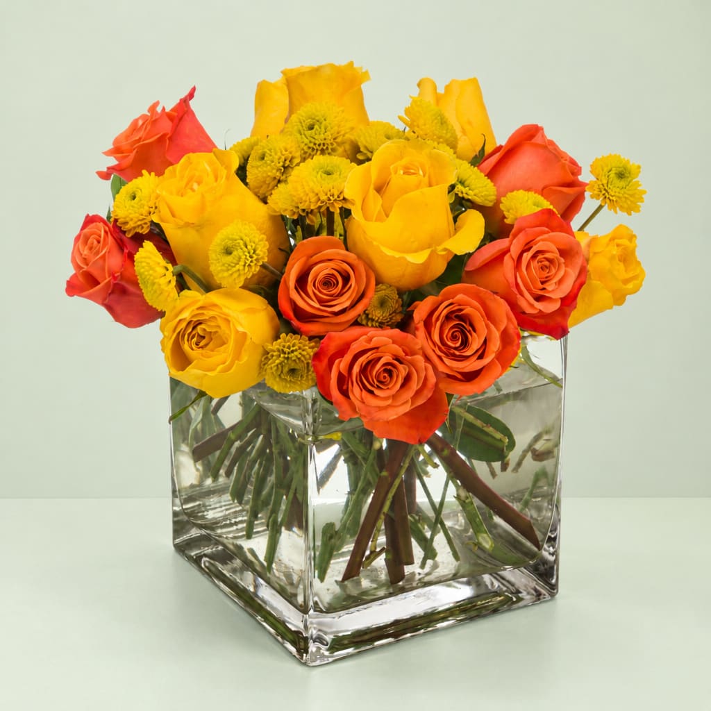 Yellow and orange roses with small yellow mums in a square glass vase