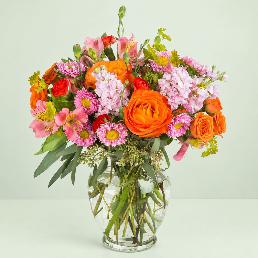 Mixed bouquet of orange, pink, and red flowers in a clear glass vase
