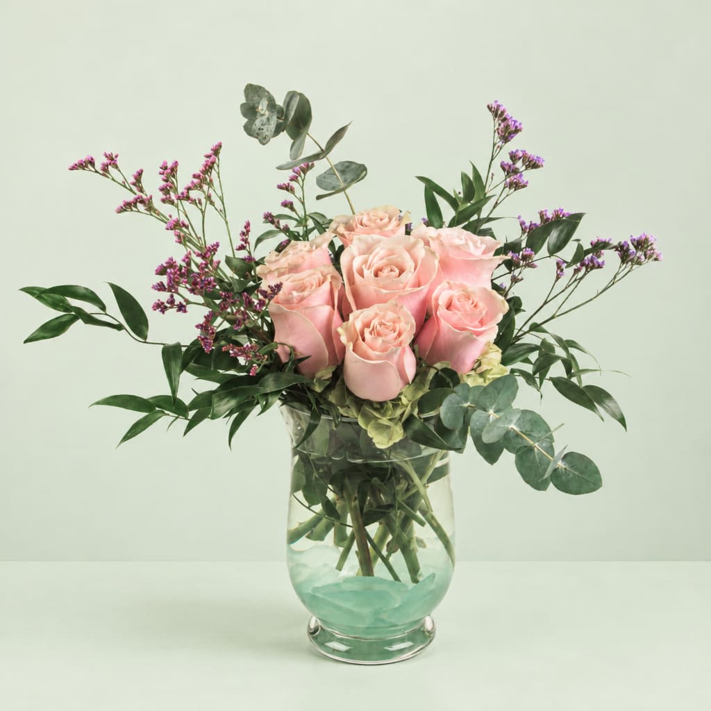 Pink roses in a clear glass vase with purple filler flowers
