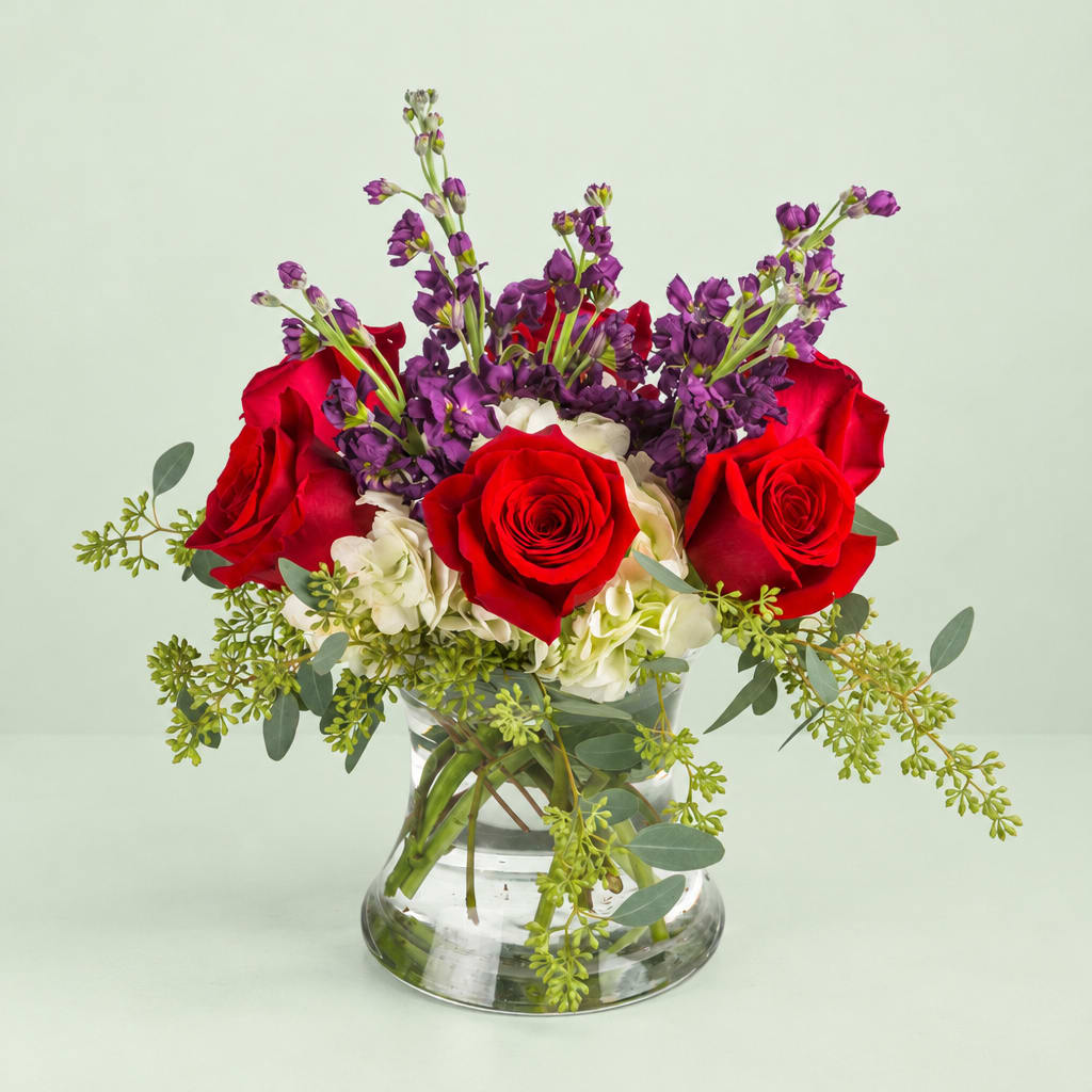 Red roses and purple flowers arranged in a clear glass vase