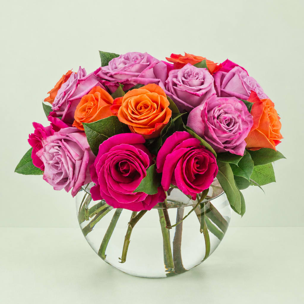 Mixed roses in pink, lavender, and orange arranged in a clear glass vase
