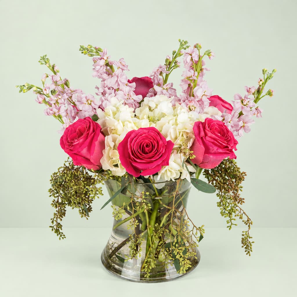 Pink roses and white hydrangeas in a clear glass vase with trailing greenery