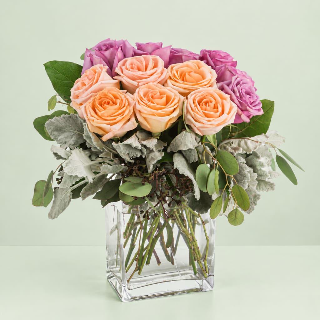 Peach and purple roses arranged in a clear glass vase