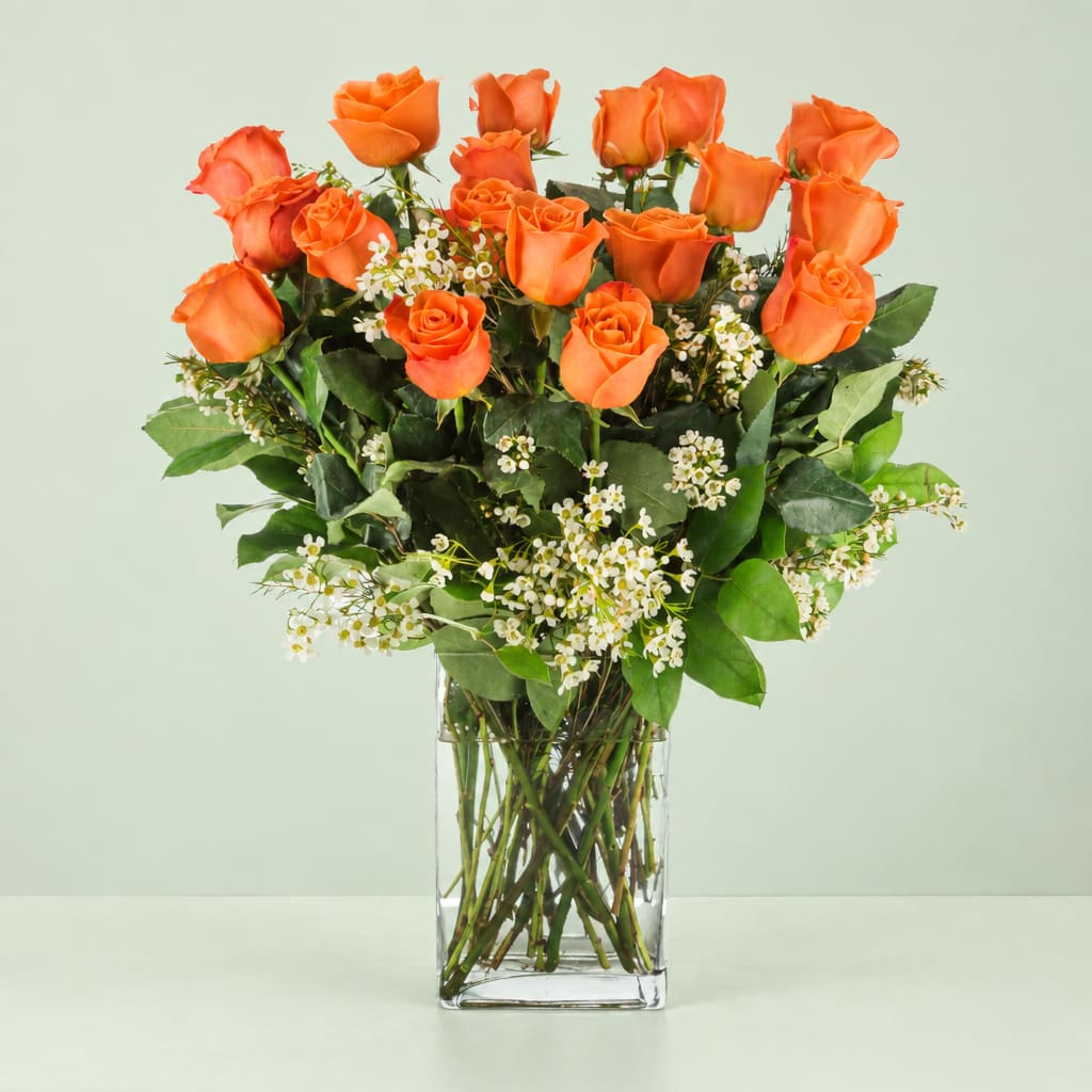 Orange roses in a clear glass vase with small white filler flowers