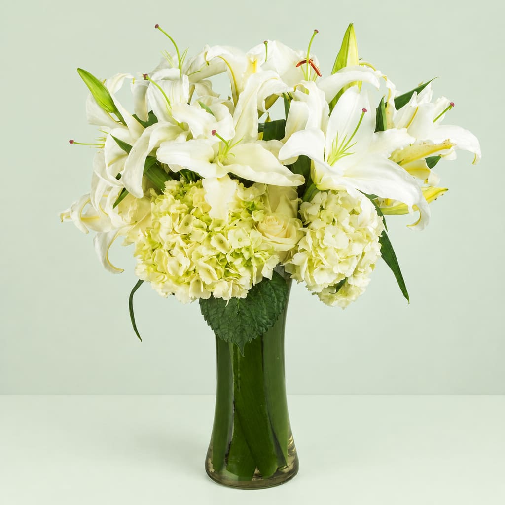 White lilies and pale hydrangeas arranged in a tall glass vase