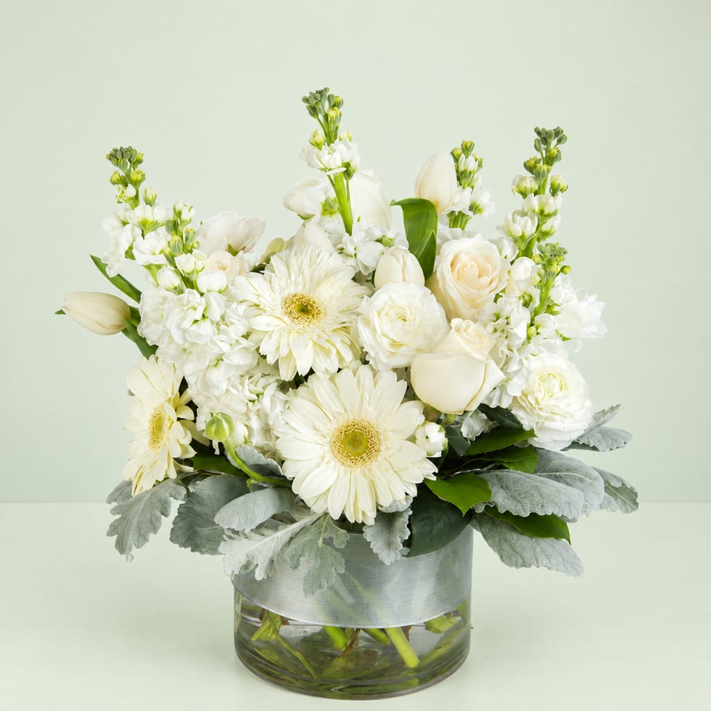 White floral arrangement in a glass vase with gerbera daisies and roses