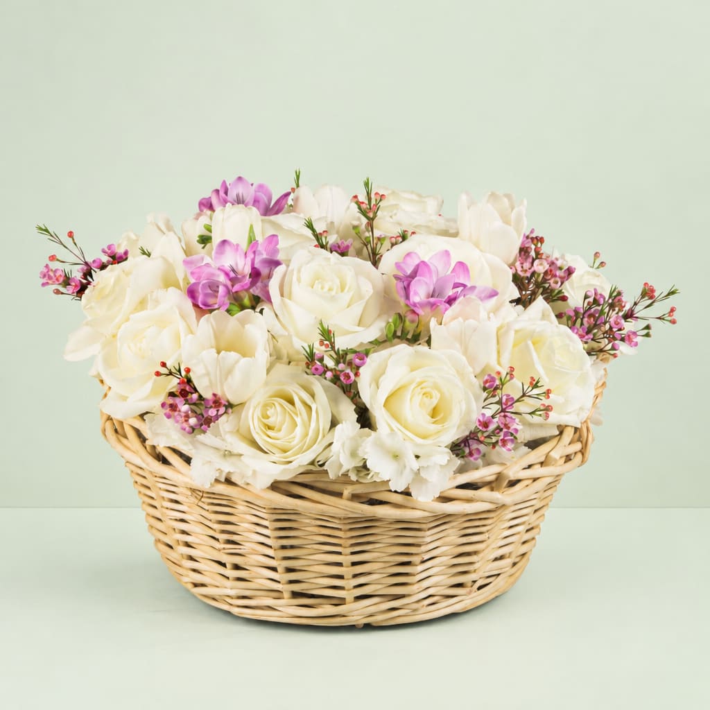 White roses and purple blooms arranged in a wicker basket