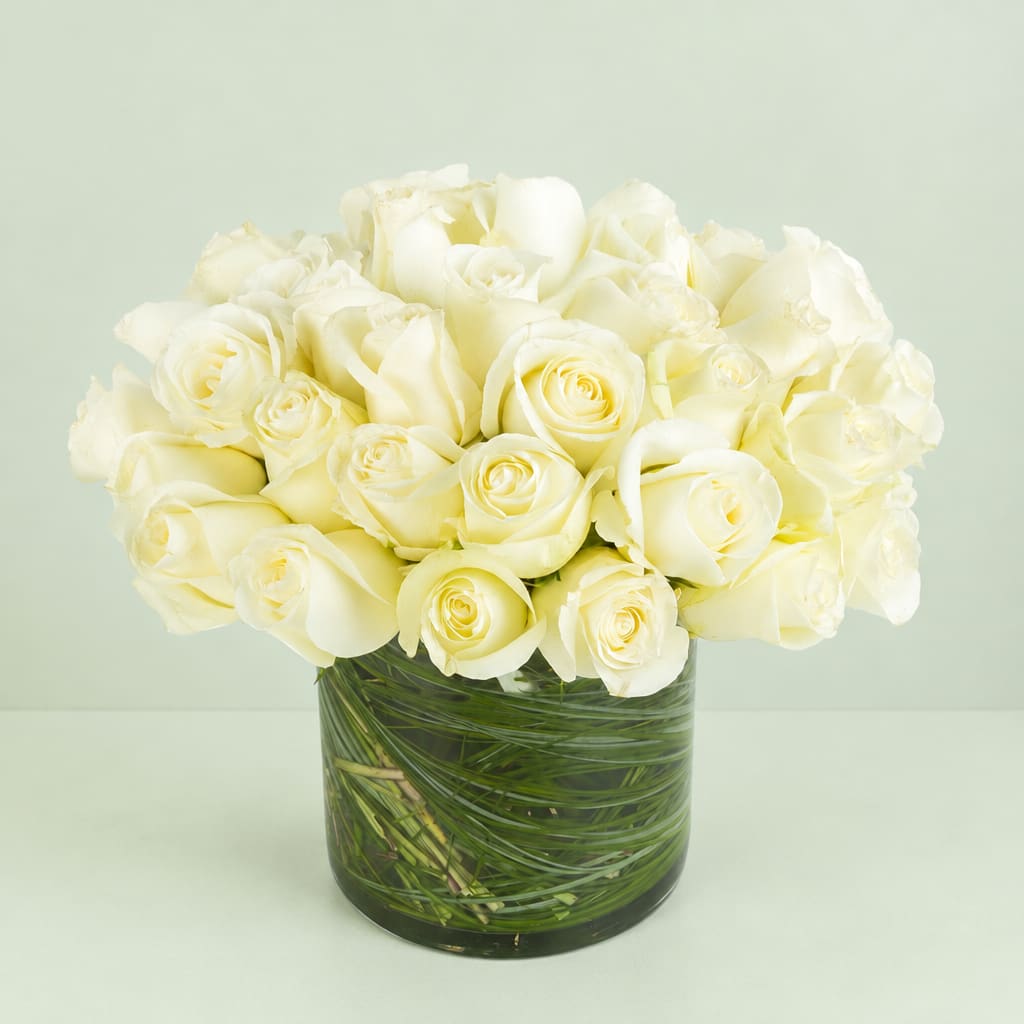 White roses arranged in a clear glass vase with green stems visible inside
