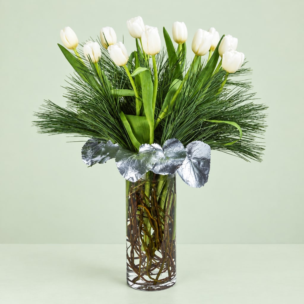 White tulips in a tall glass vase with silver leaves and pine-like greenery