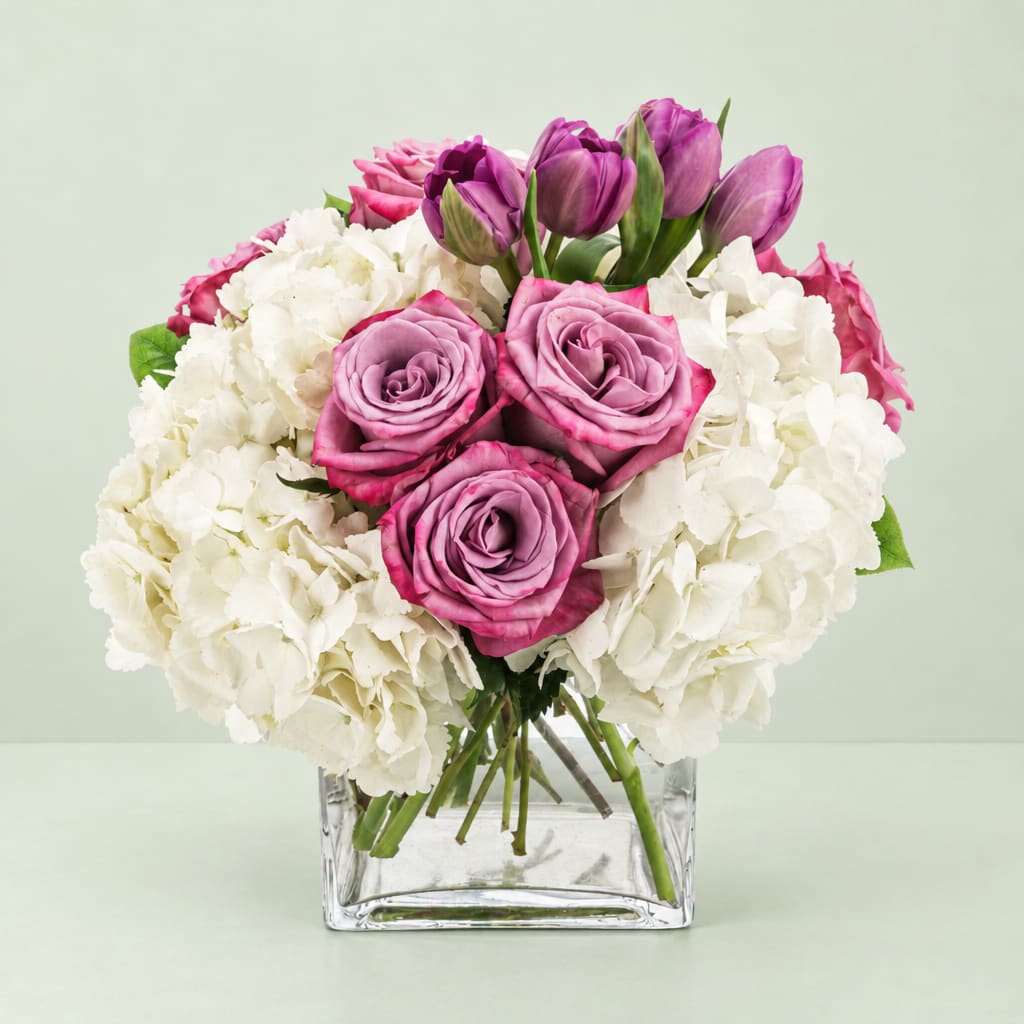 Pink roses and purple tulips in a clear square vase with white hydrangeas