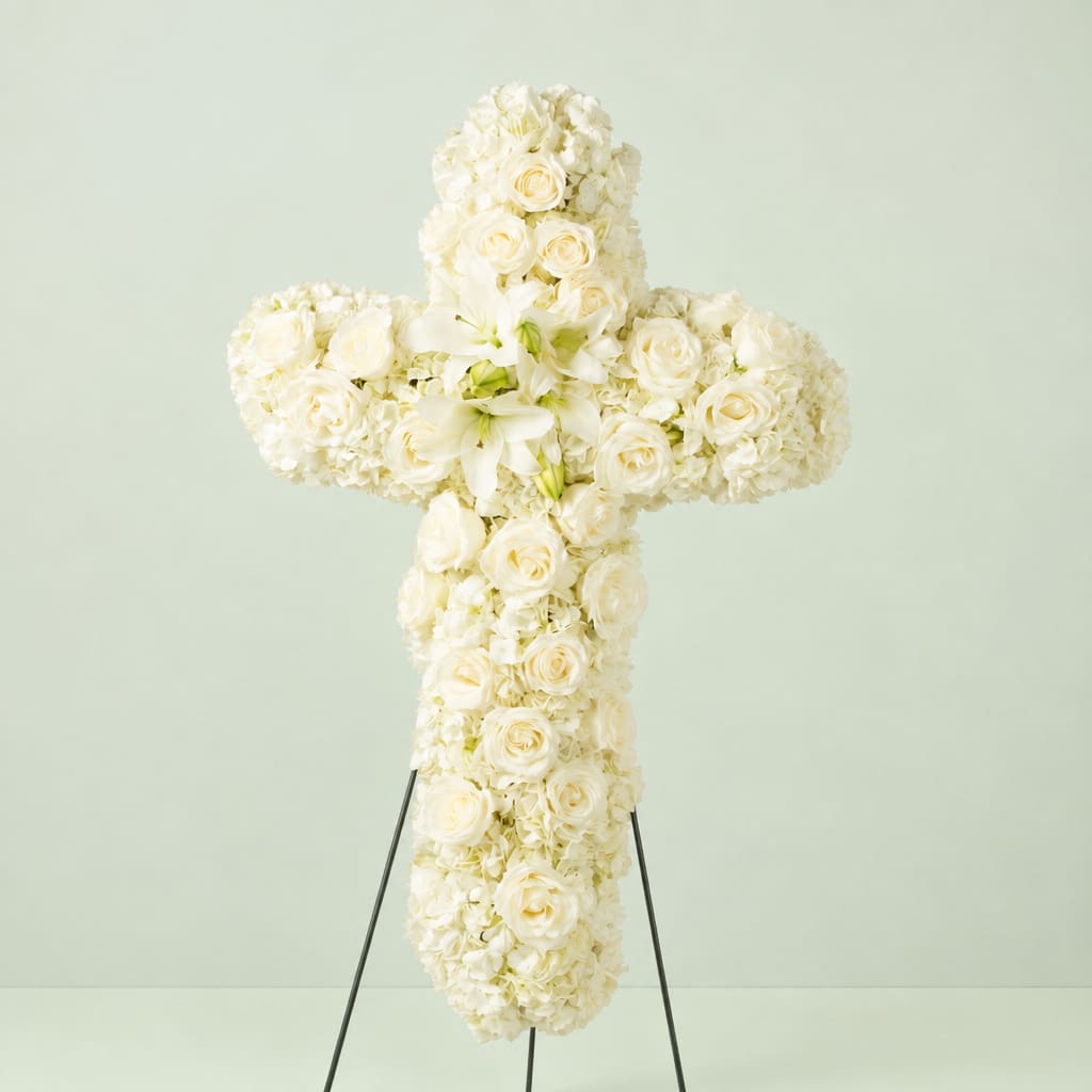 White floral cross on a stand with roses and lilies