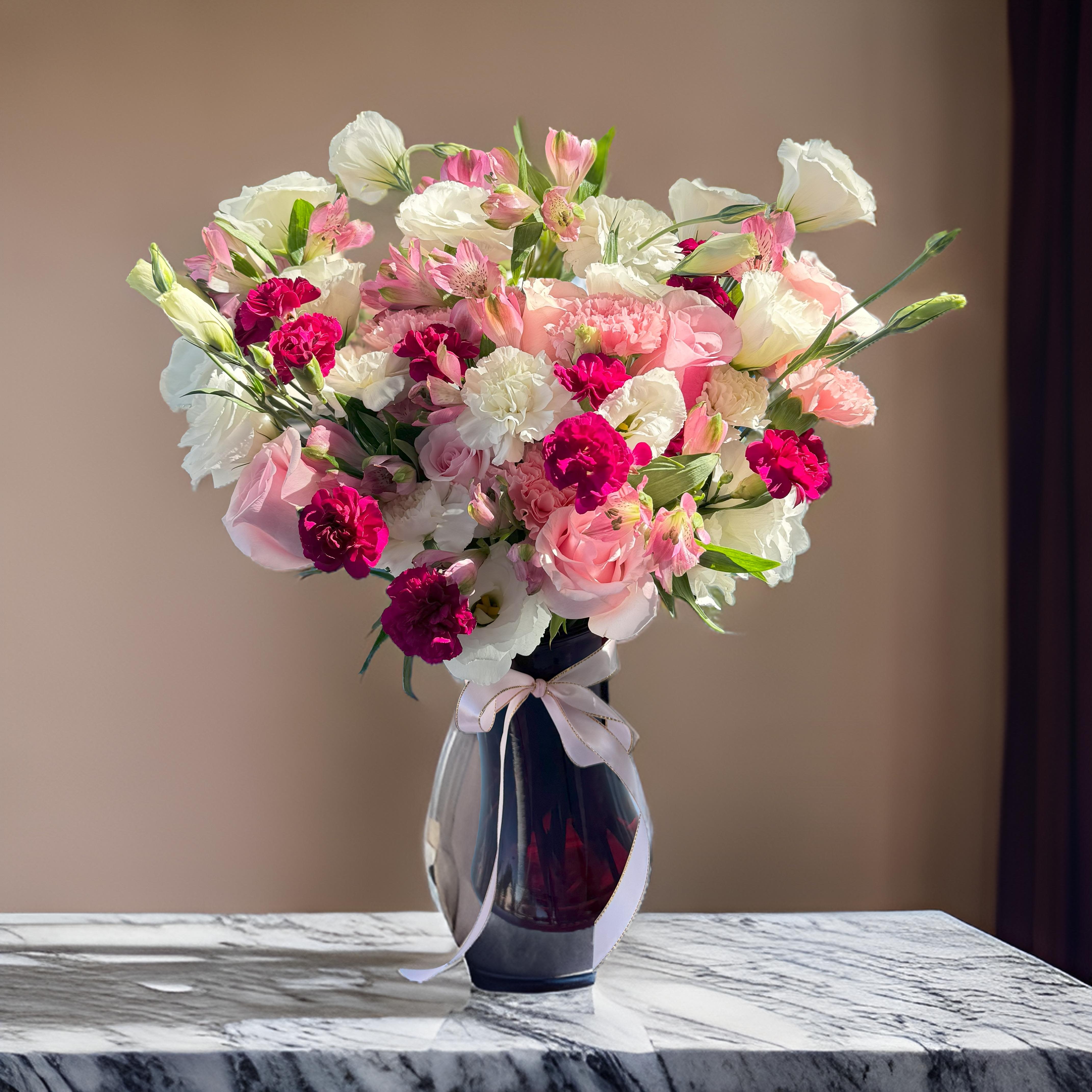 Pink and white mixed bouquet in a dark glass vase with a ribbon