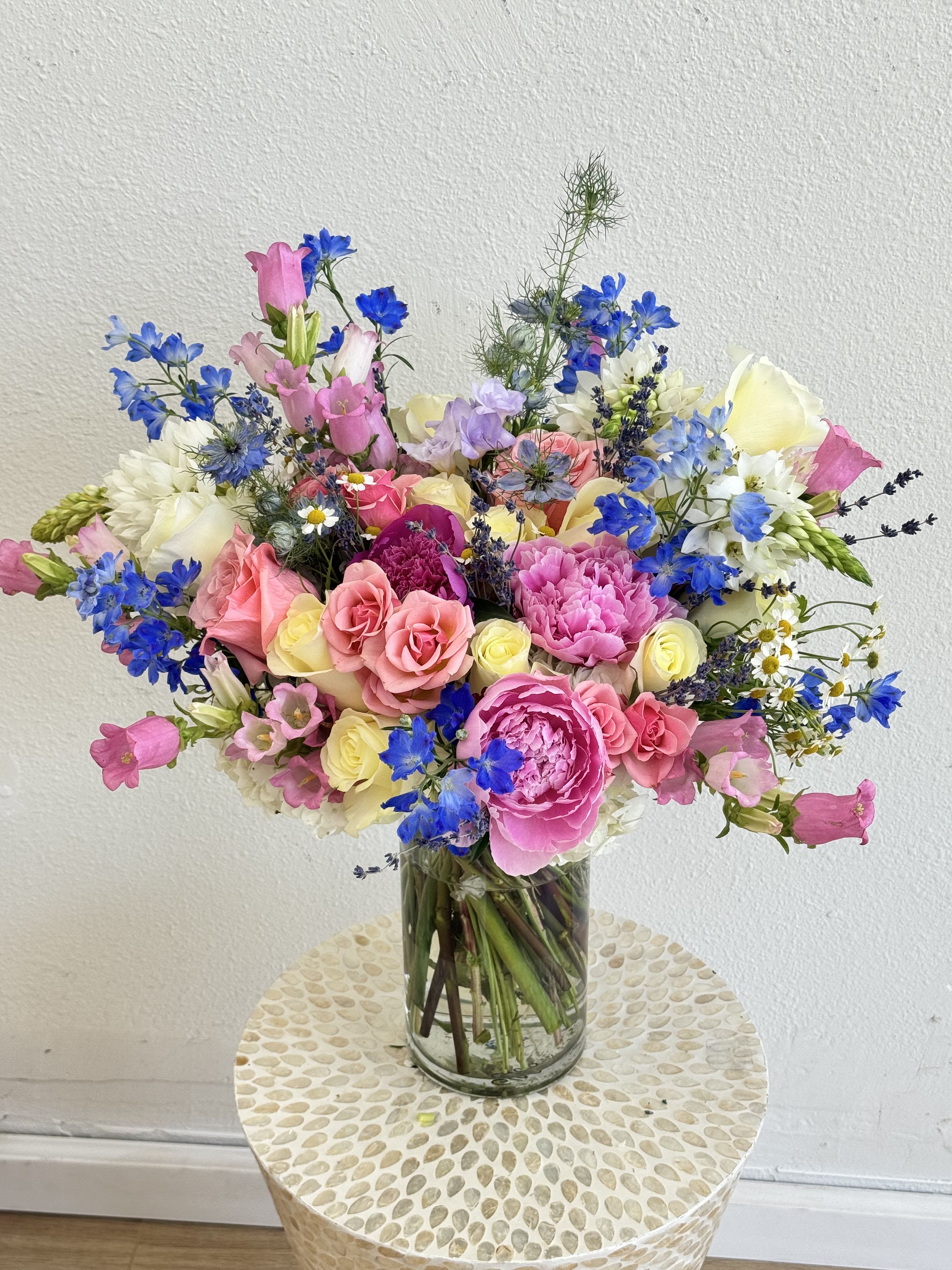 Colorful mixed bouquet of pink, blue, and white flowers in a glass vase