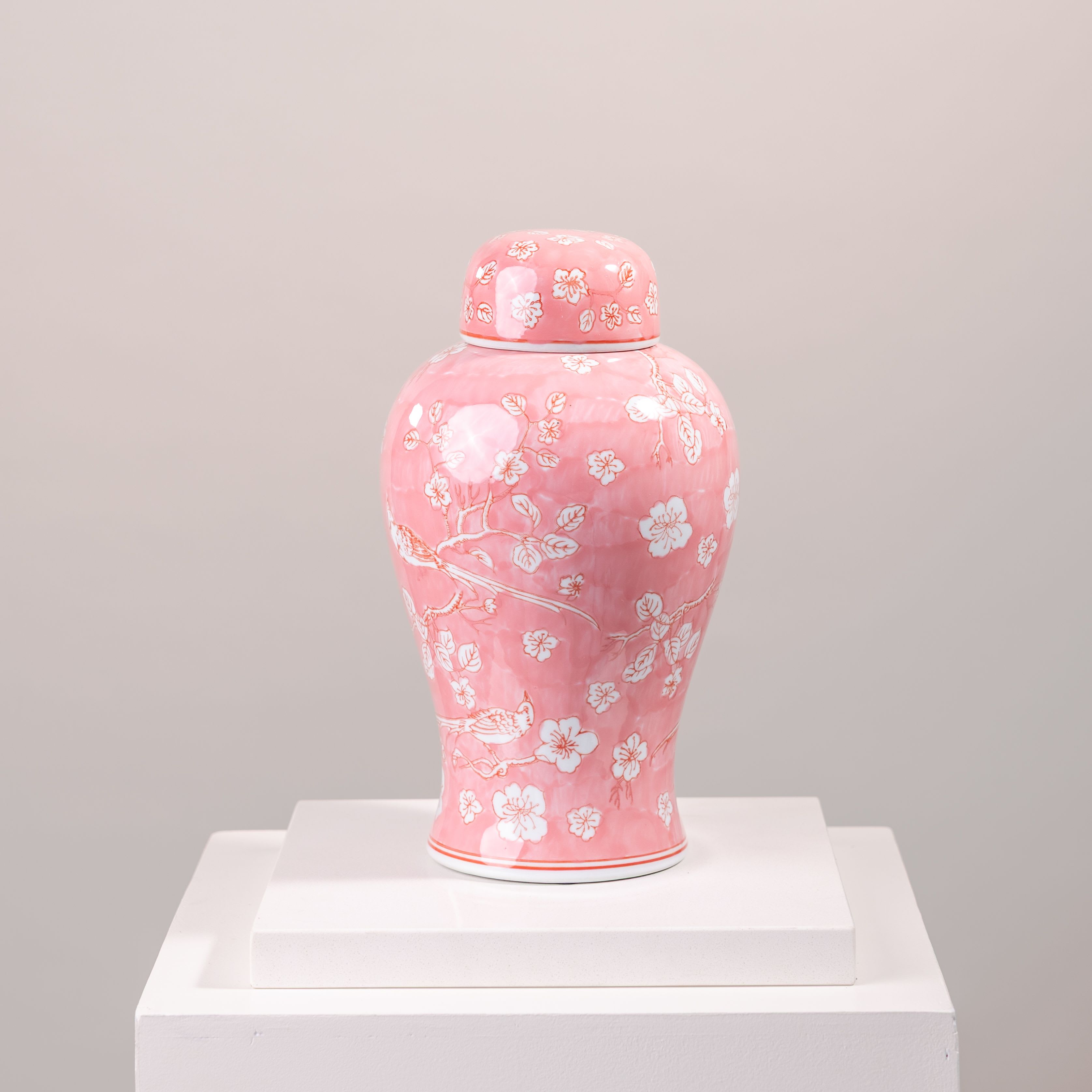 Pink ceramic jar with white floral cherry blossom pattern on a pedestal