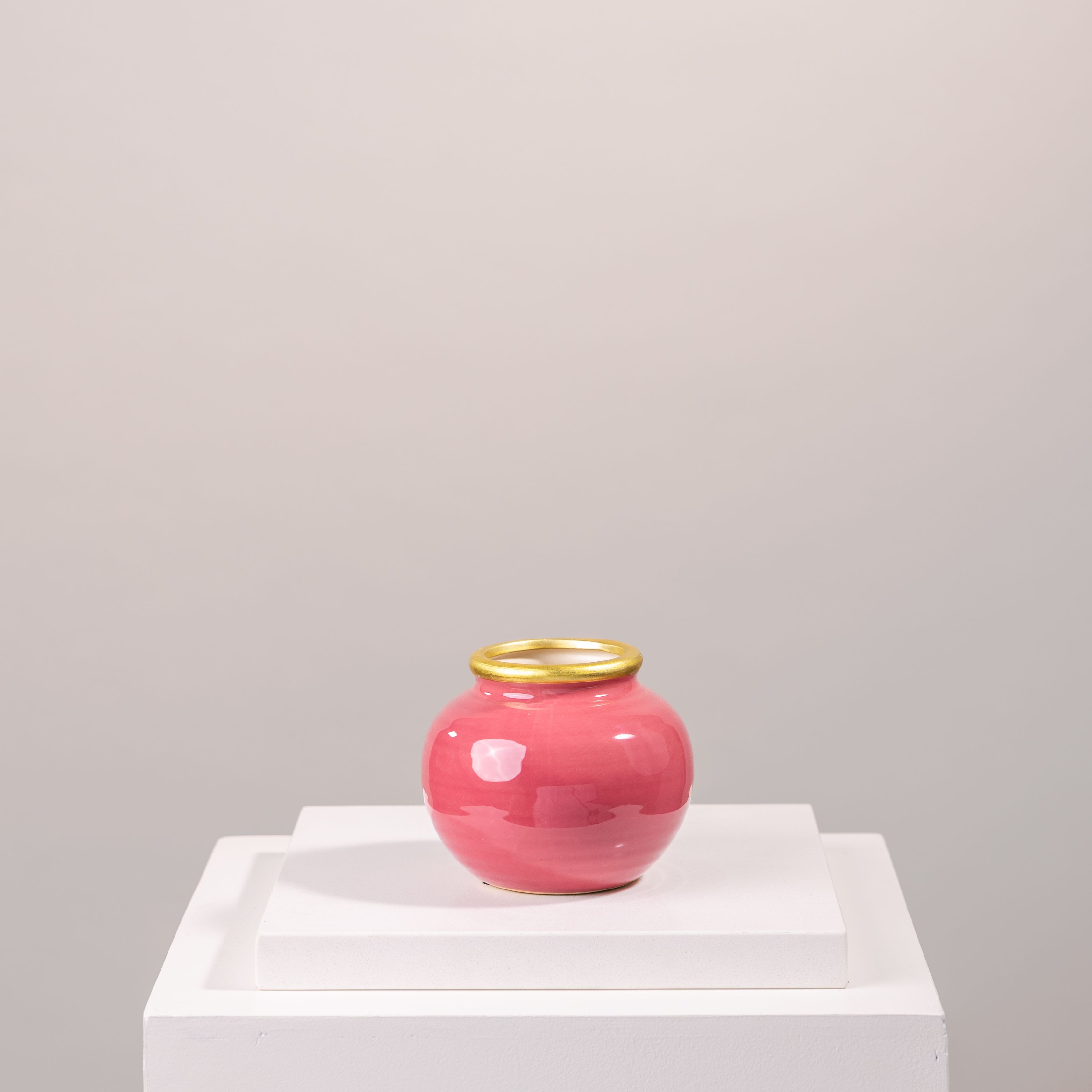 Pink ceramic vase with a gold rim on a white pedestal